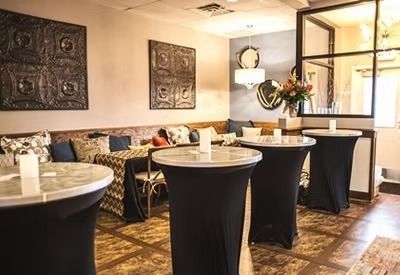 Small restaurant dining area with round tables, black table covers, patterned chairs, and warm lighting.