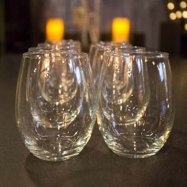 Two rows of clear stemless wine glasses on a table with warm candlelight in the background