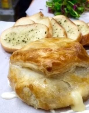 Golden baked pastry with melted cheese, alongside sliced bread on a plate