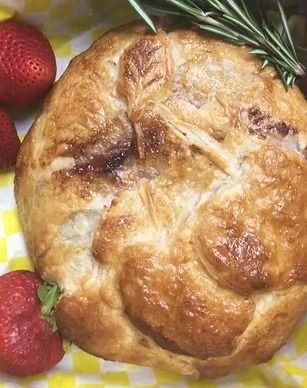 Golden-brown baked pastry with strawberries and a rosemary sprig on a checkered cloth