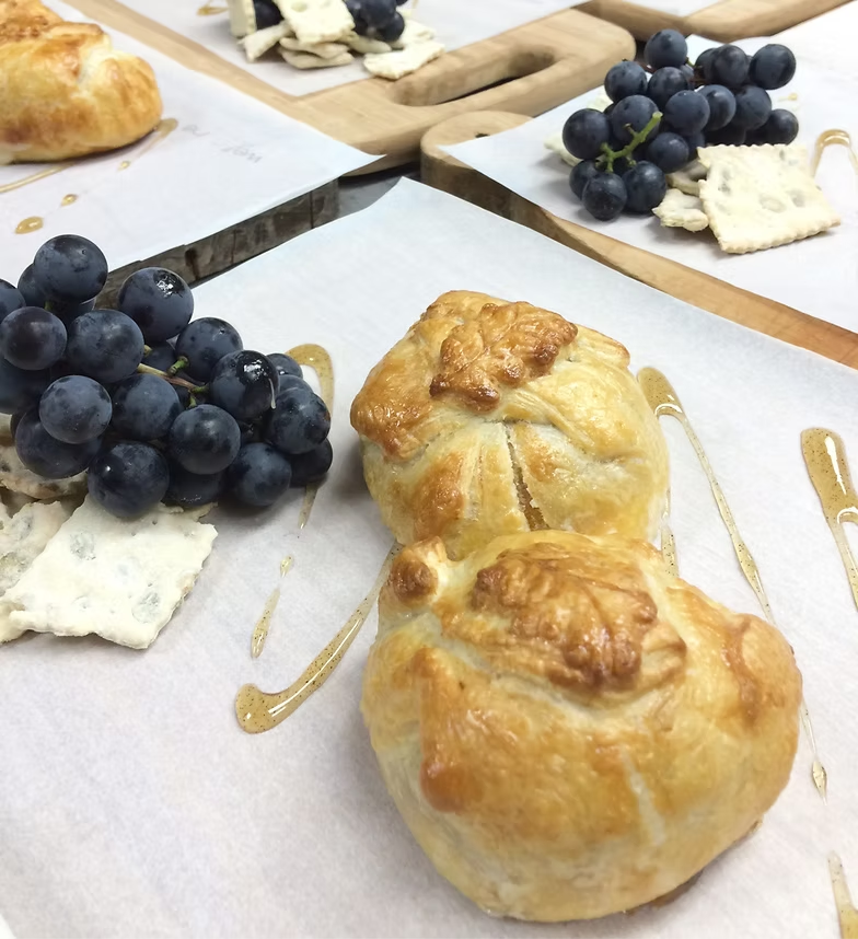 Grapes, cheese, and golden pastries on white plates at a buffet table