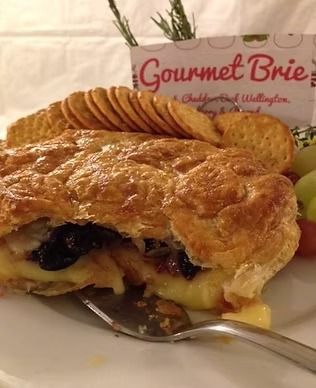 Berry-filled pastry with a golden crust on a plate, topped with sliced almonds and a “Gourmet Brie” sign behind it