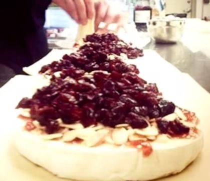Person topping a cheesecake with dark berries on a kitchen counter