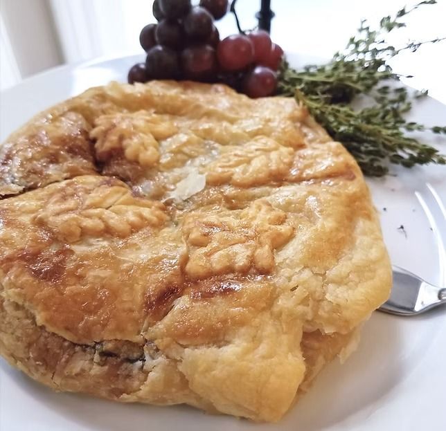Golden baked pastry on a white plate with grapes and herbs garnish