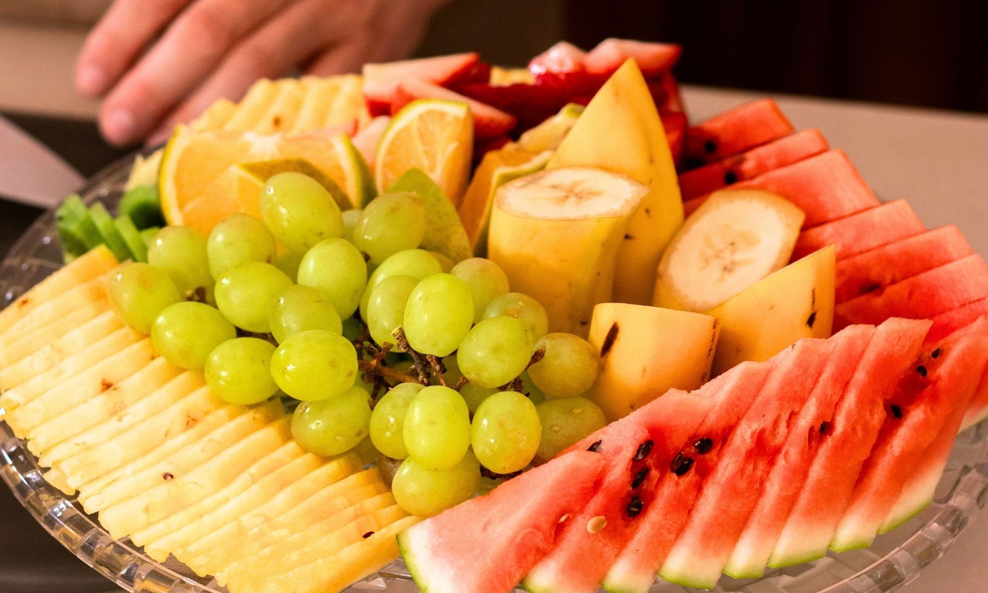 Fruit platter with sliced watermelon, green grapes, bananas, apples, and melon arranged on a tray