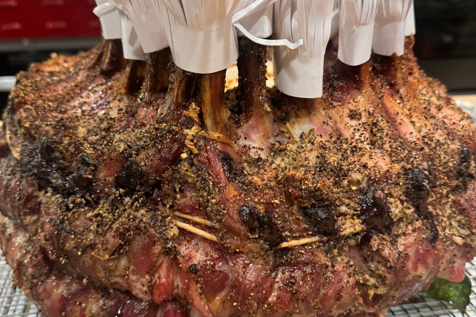 A large roasted meat platter with browned crust and skewered handles on a wire rack