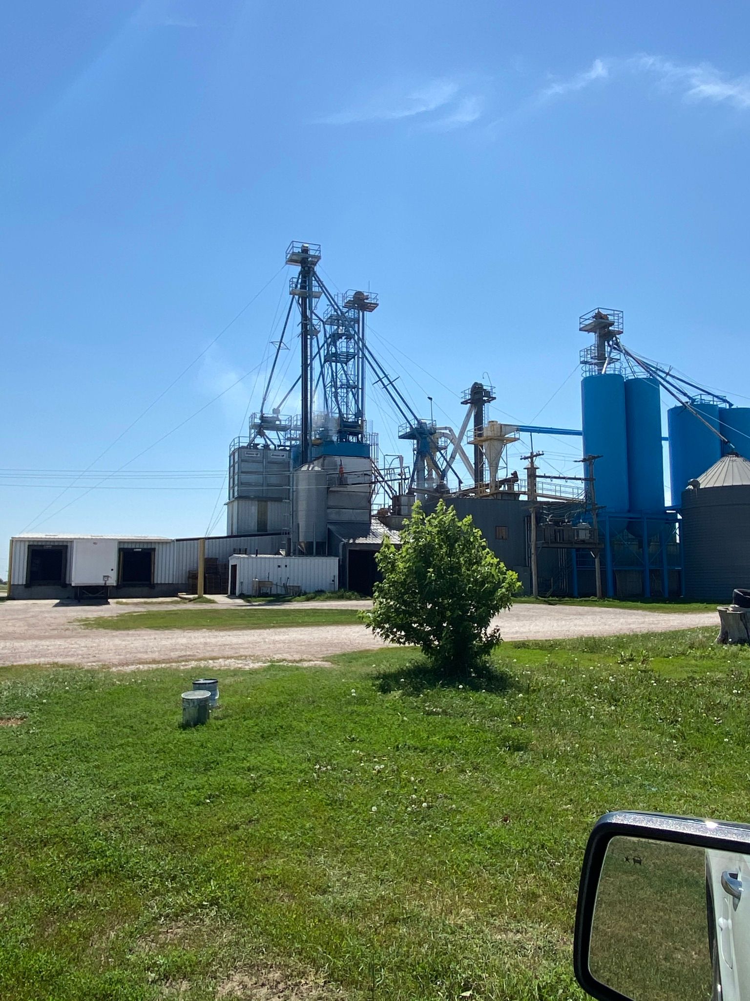 Grain elevator complex with blue silos and support structures under a clear sky - before