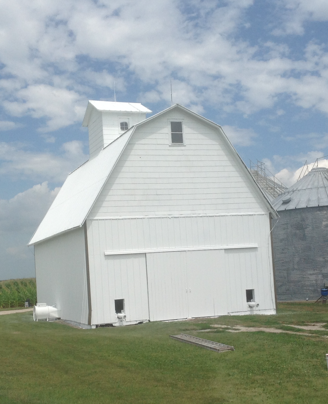 White barn with a gambrel roof on a grassy farm under a partly cloudy sky