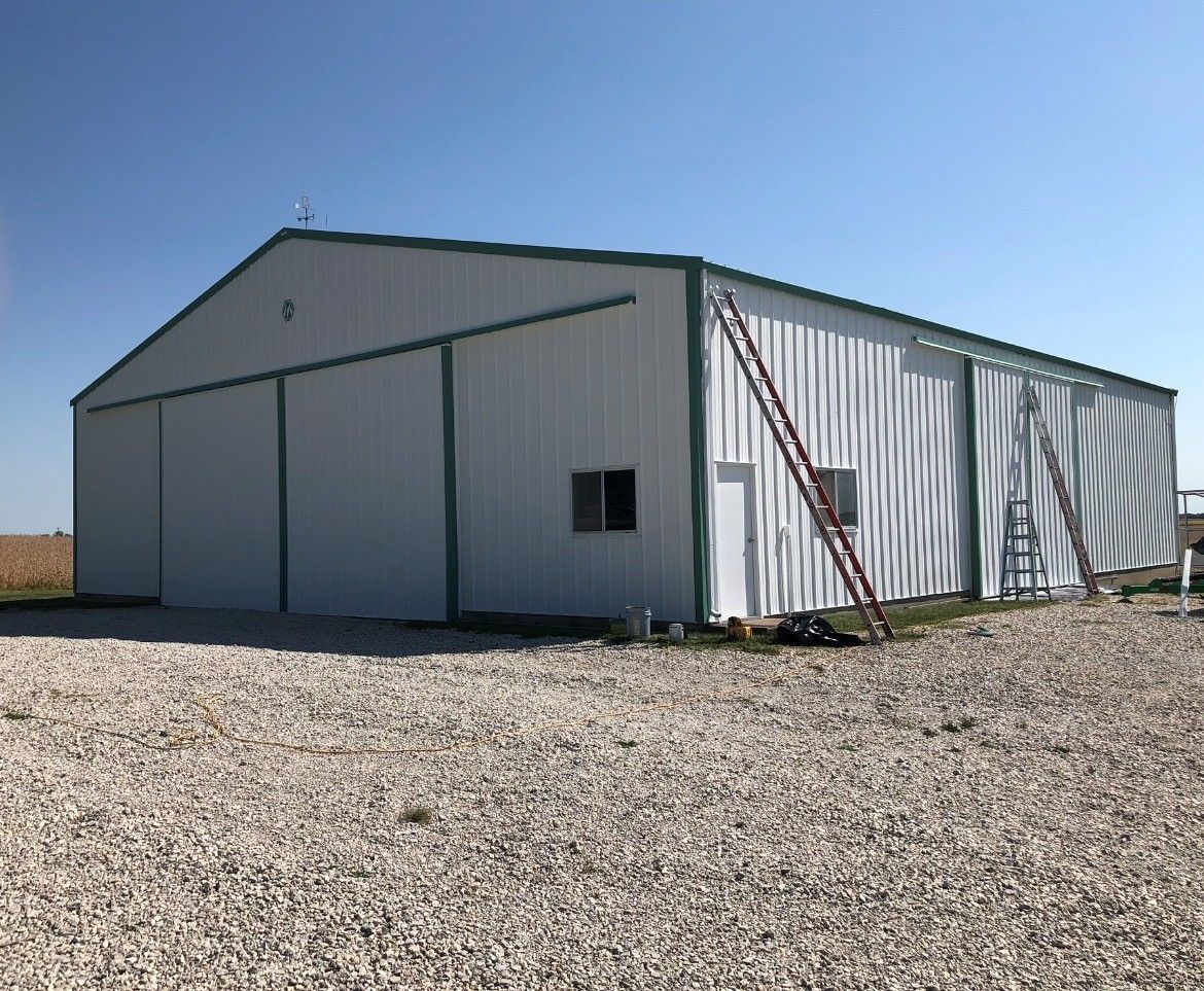 Large white metal storage building on a gravel lot under a clear blue sky, with a ladder on the side.