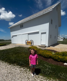 Girl standing outside a white barn on a sunny day