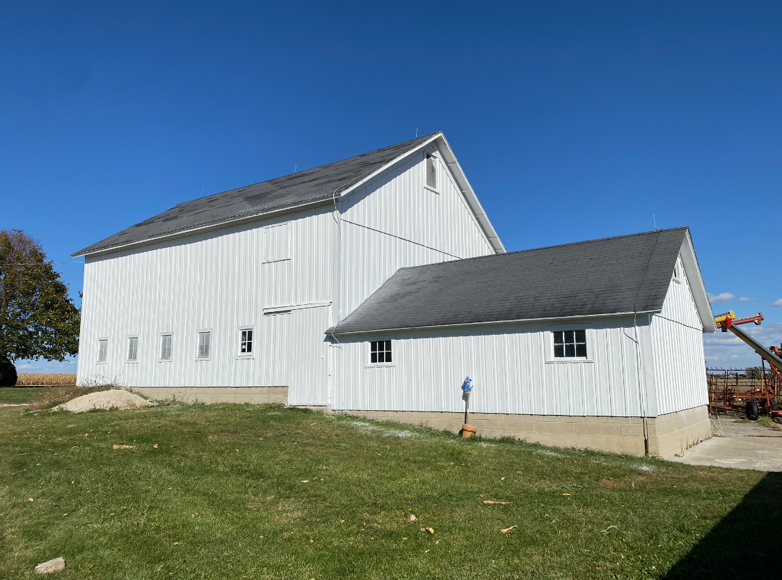 White barn with gray roof on a grassy hill under a clear blue sky.