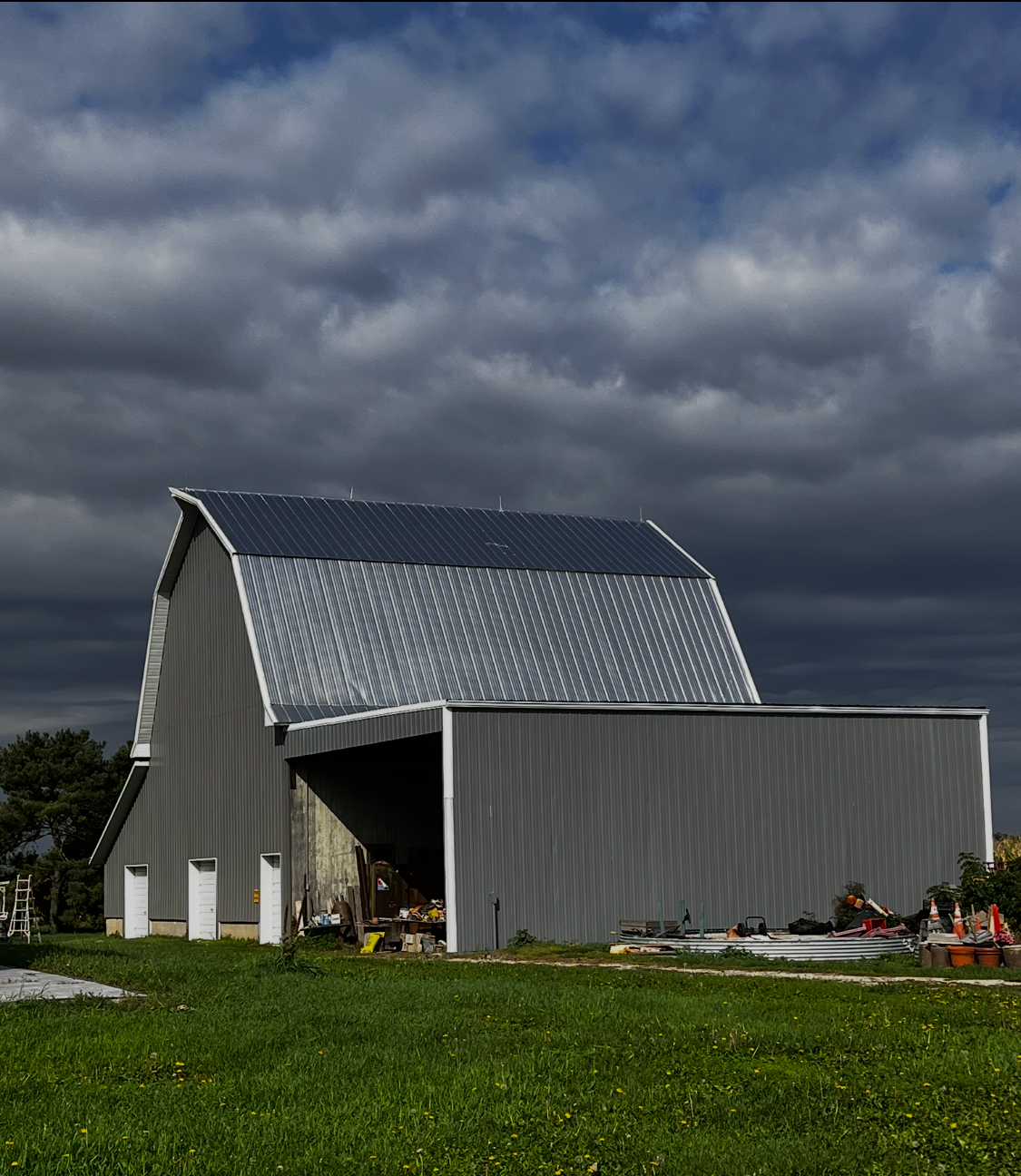 Gray barn with a metal roof in a grassy field under dark, cloudy sky
