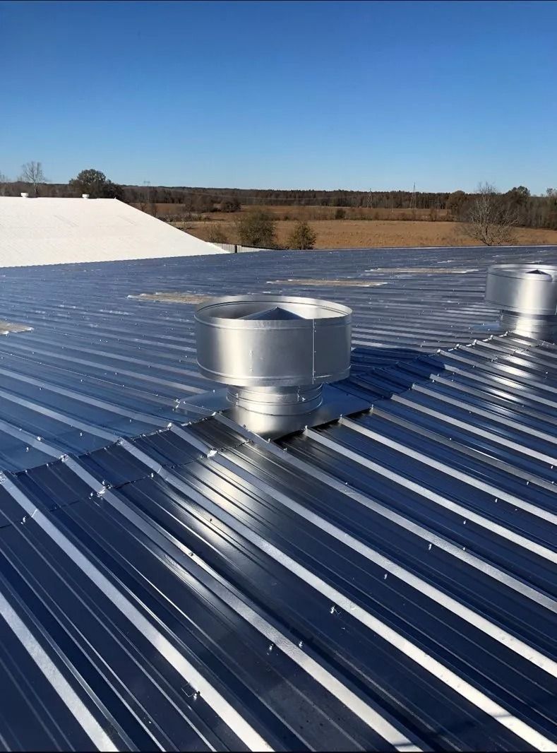 Metal roof with cylindrical vent, blue sky.