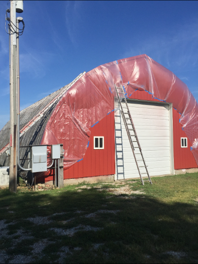 Red barn partially covered in red plastic, ladder leaning against the white garage door.