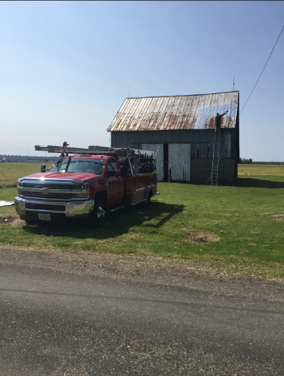 Red pickup truck parked near a weathered barn on a grassy field under a bright sky.