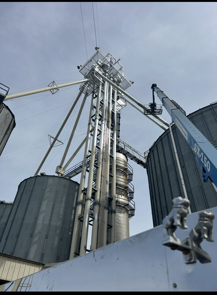 Grain elevator tower with silos, under a cloudy sky. A lift is near the structure.