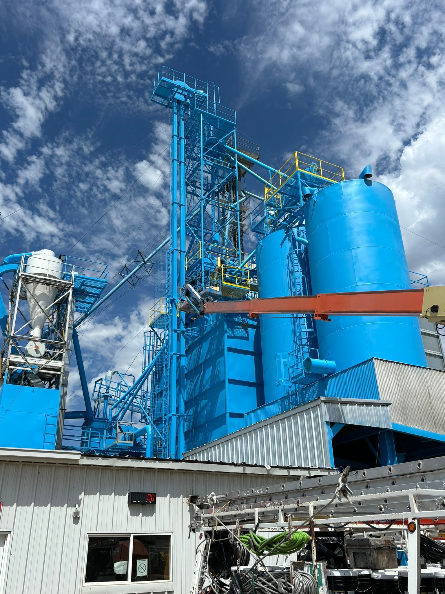 Blue industrial plant with tanks and towers against a cloudy sky.