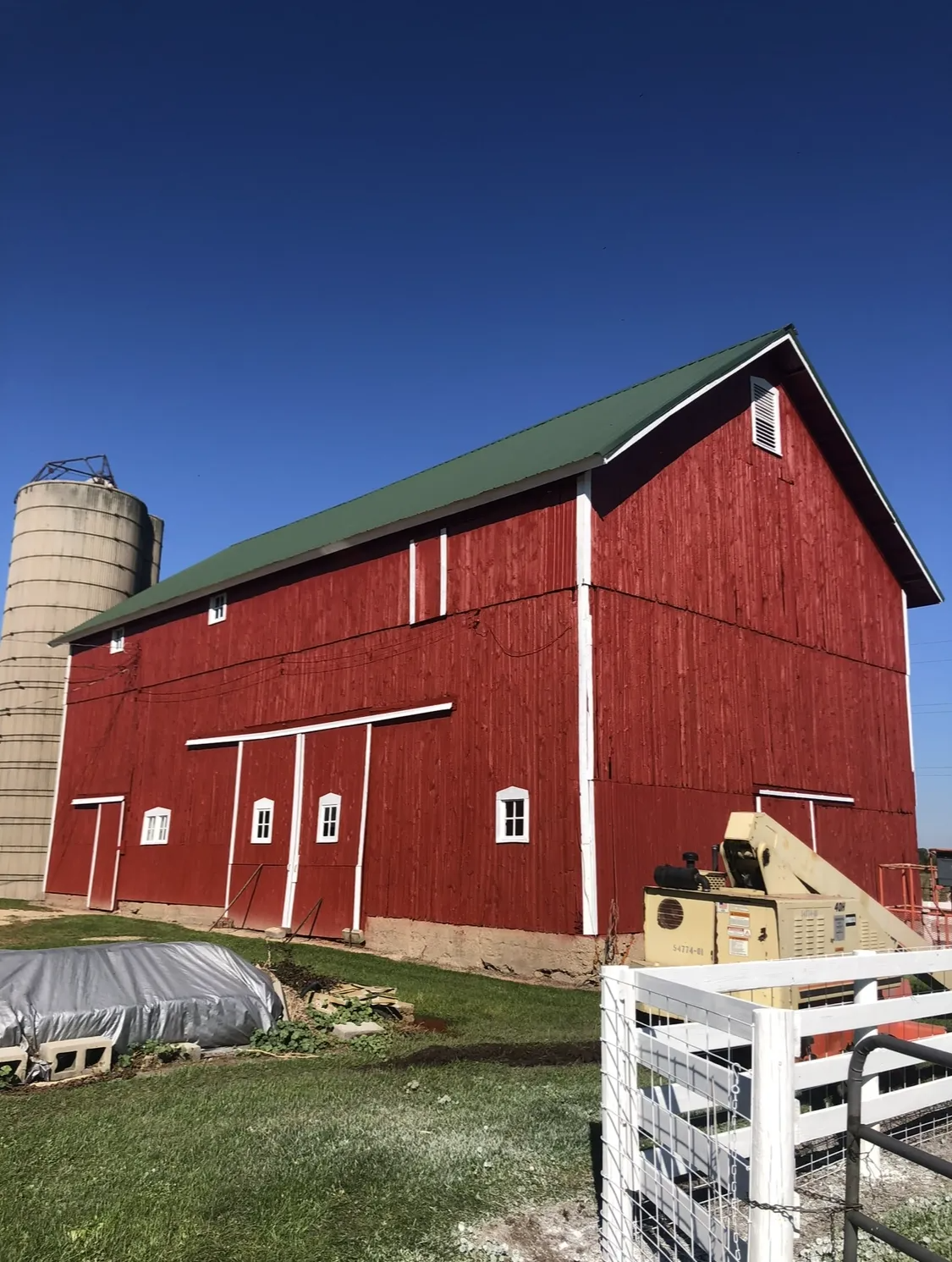 Red barn with green roof and silo under a clear blue sky.