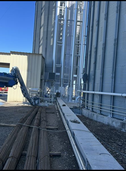 Exterior view of a tall grain silo with a conveyor belt and auger system.