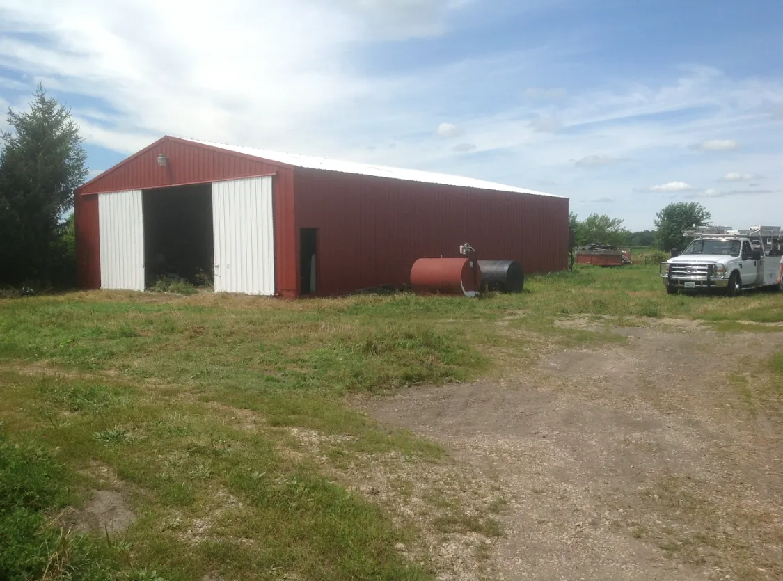 Red barn with white trim and open door on grassy lot; truck parked nearby.
