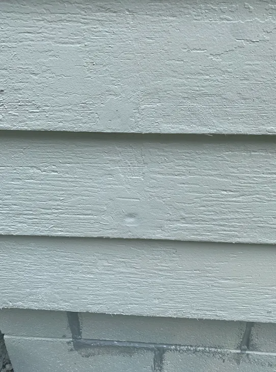Light blue siding with a small dent, above a brick foundation.