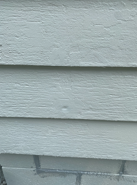 Light blue siding with a small dent, above a brick foundation.