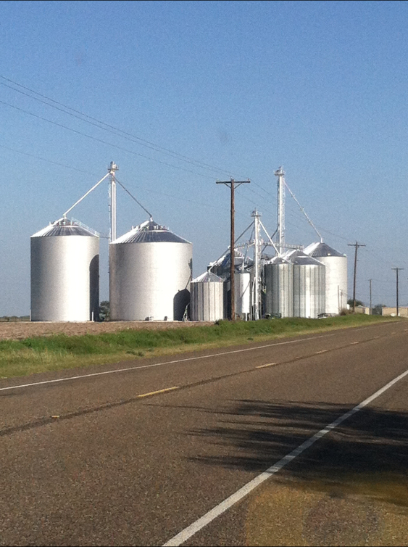 Silver grain silos along a road, under a clear blue sky.