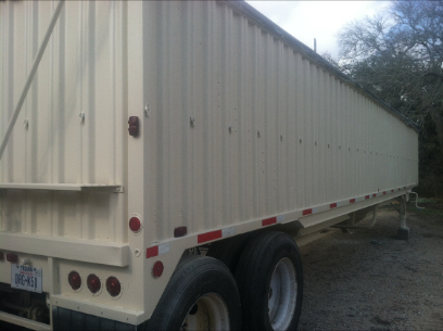 Tan grain trailer with vertical ridged sides, tires, and red reflector lights.