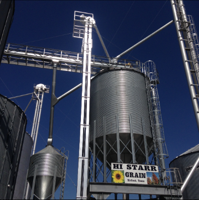 Grain storage facility with tall metal silos and elevators against a blue sky.