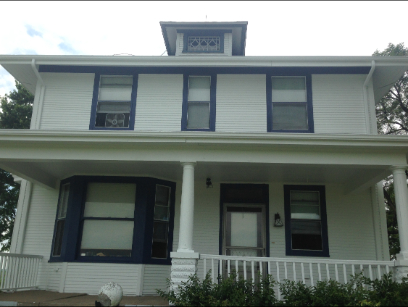 Two-story white house with blue trim, porch, and a small upper level with decorative elements.