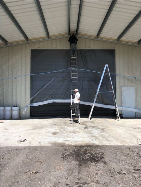 Person on ladder inside industrial building, adjusting fabric above large door.