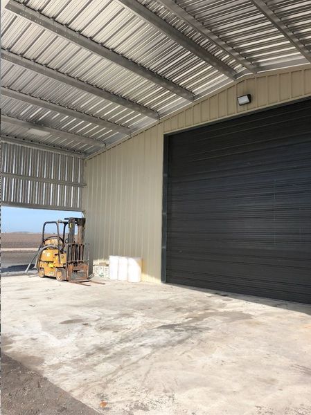 Interior of a metal warehouse with a closed black garage door, a forklift, and concrete flooring.