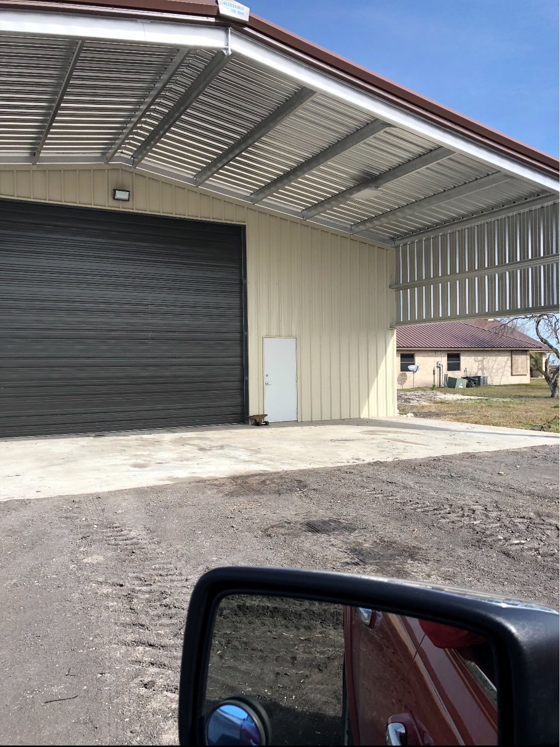 Building with large black garage door, covered metal awning. Light beige walls. White door.