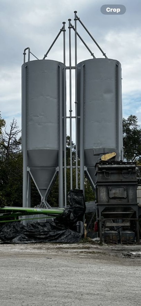 Two gray storage silos stand side-by-side with supporting metal framework against a cloudy sky.