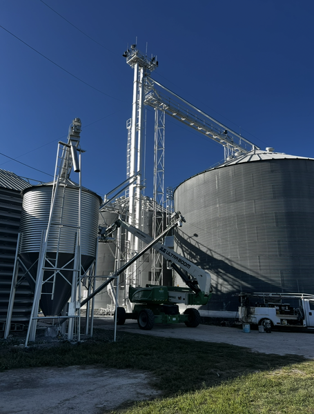 Grain elevator with silos, conveyors, and lift equipment under a blue sky.
