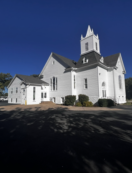 White church building with steeple, under a bright blue sky.