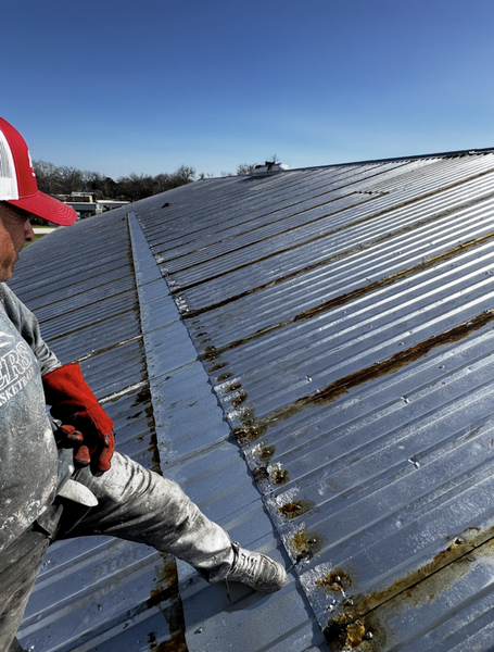 Person on a metal roof, installing a strip along the seam. Clear, sunny sky.