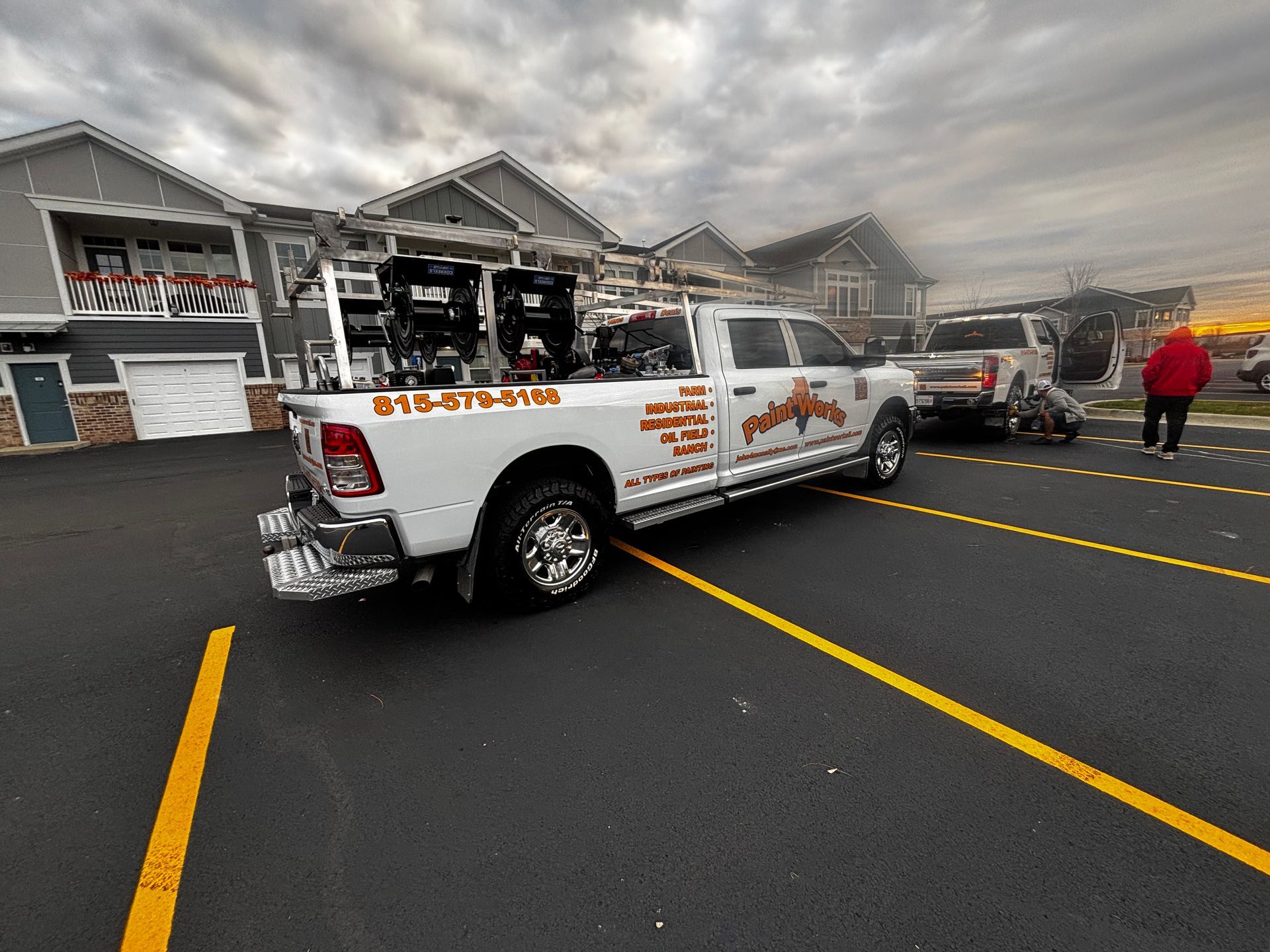 White tow truck at an apartment complex, a damaged vehicle nearby. Cloudy sky.