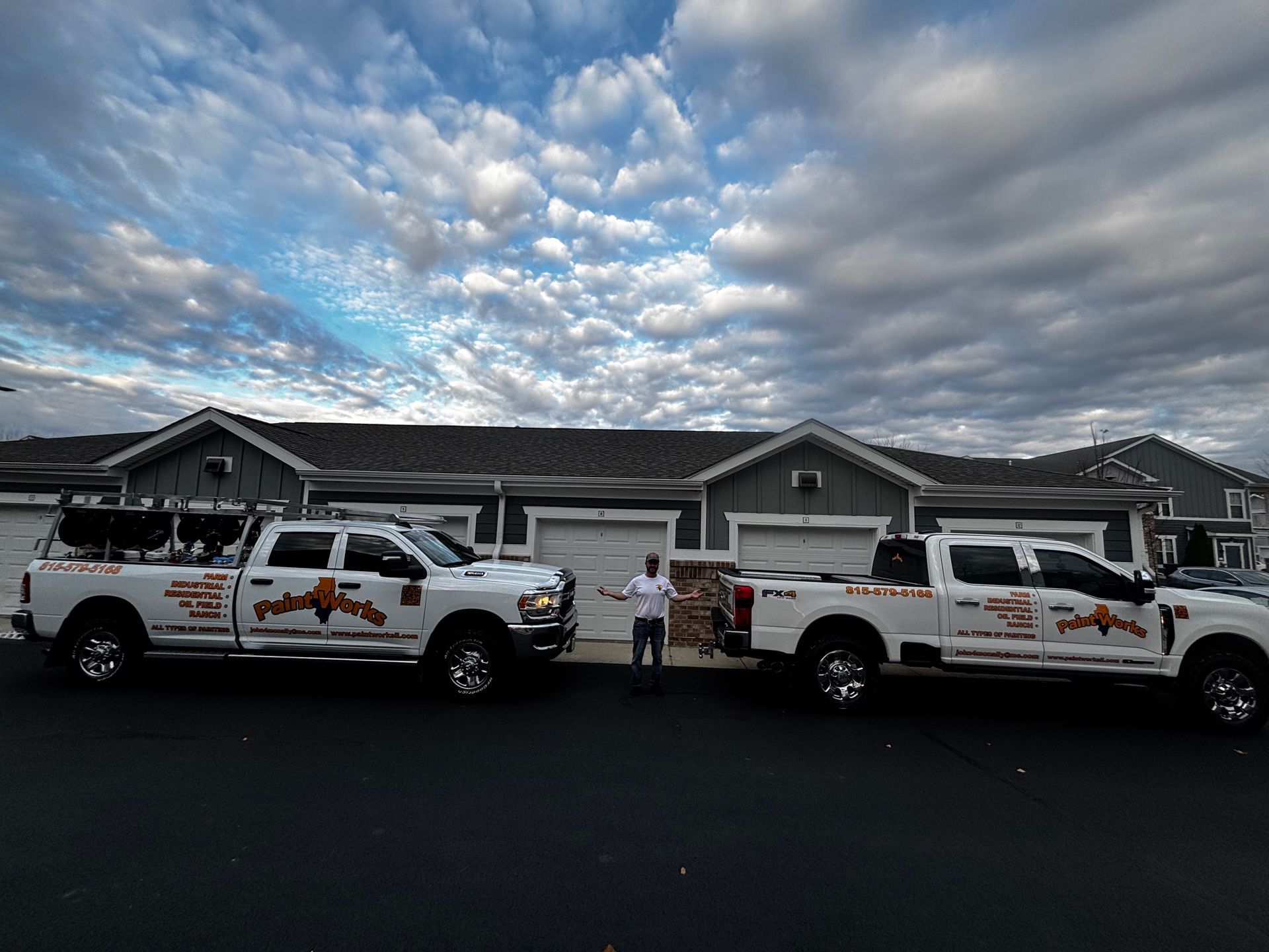 Two white work trucks parked in front of townhouses; a person stands between them. Cloudy sky.