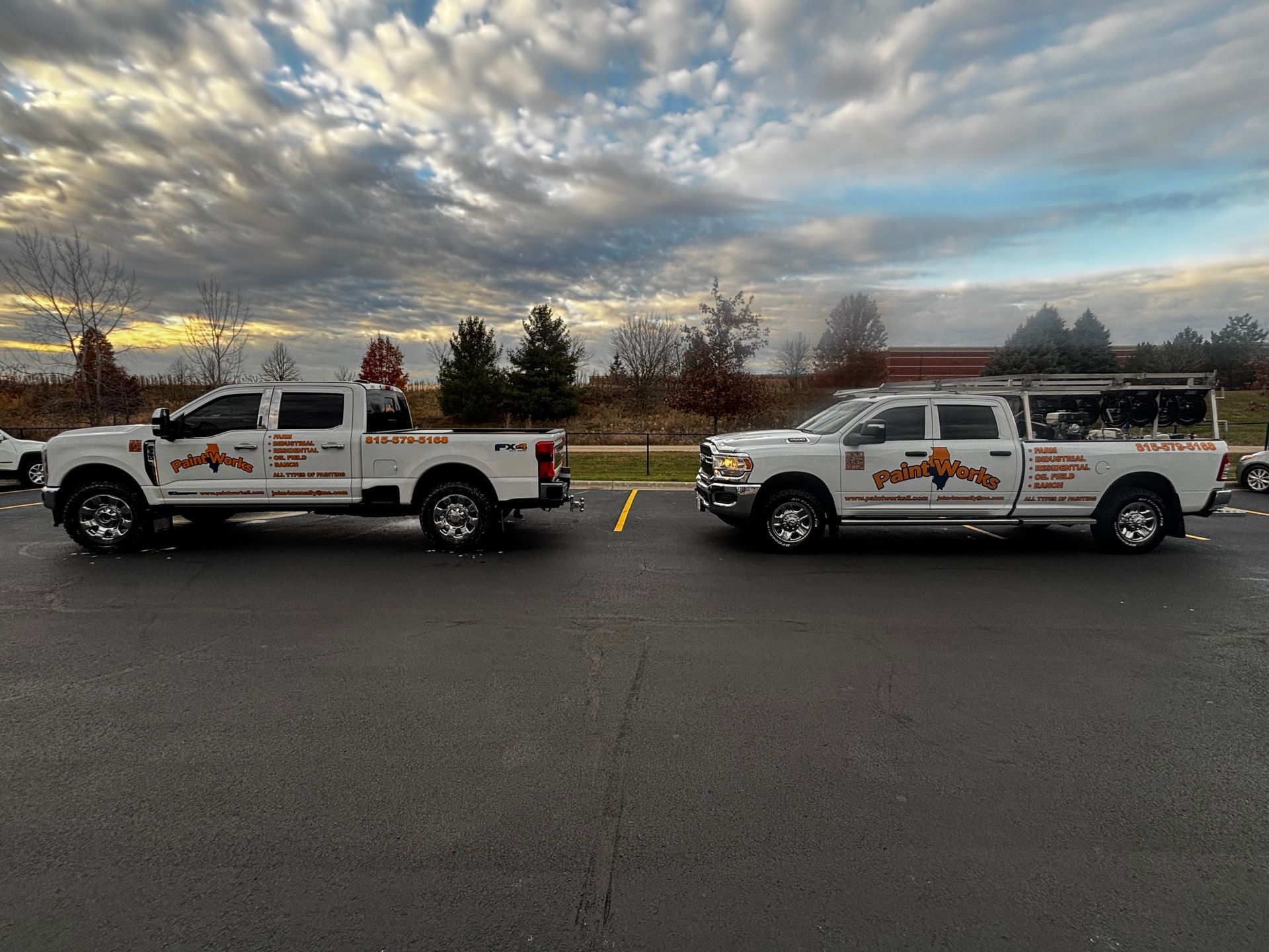Two white work trucks parked in a lot under a cloudy sky.