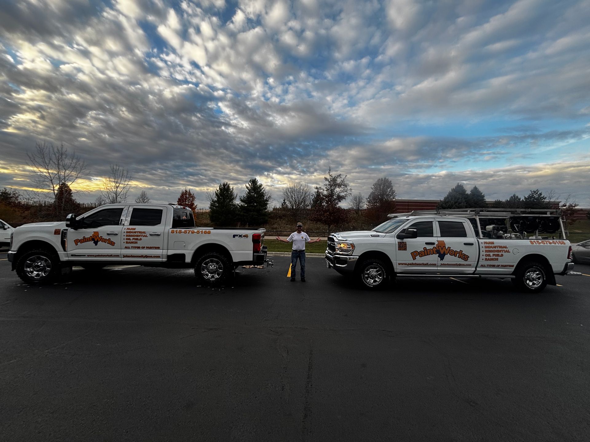 Two white trucks flank a person holding a yellow object in a parking lot under a cloudy sky.