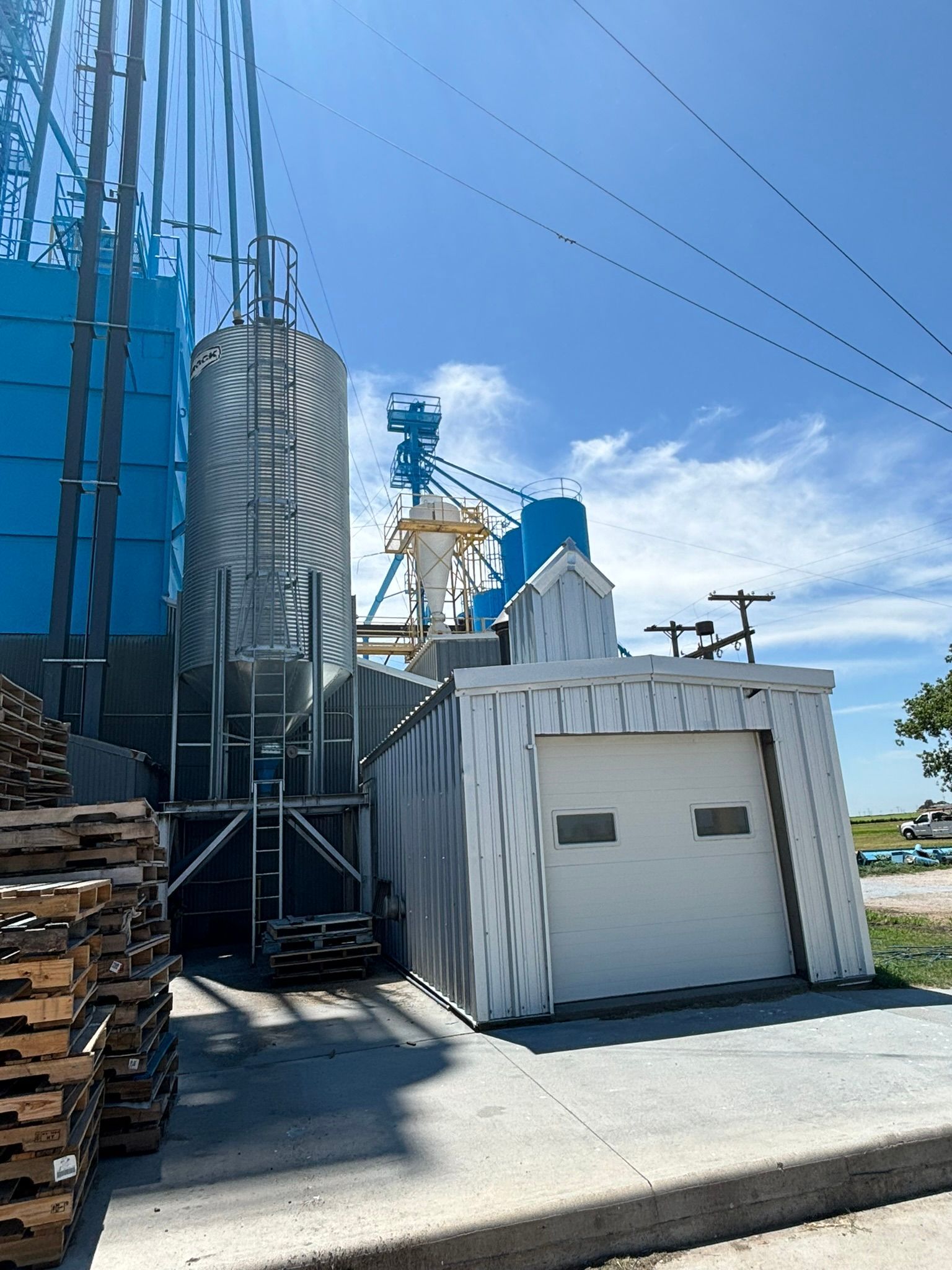Grain silo complex with blue and silver structures, garage, and clear sky.