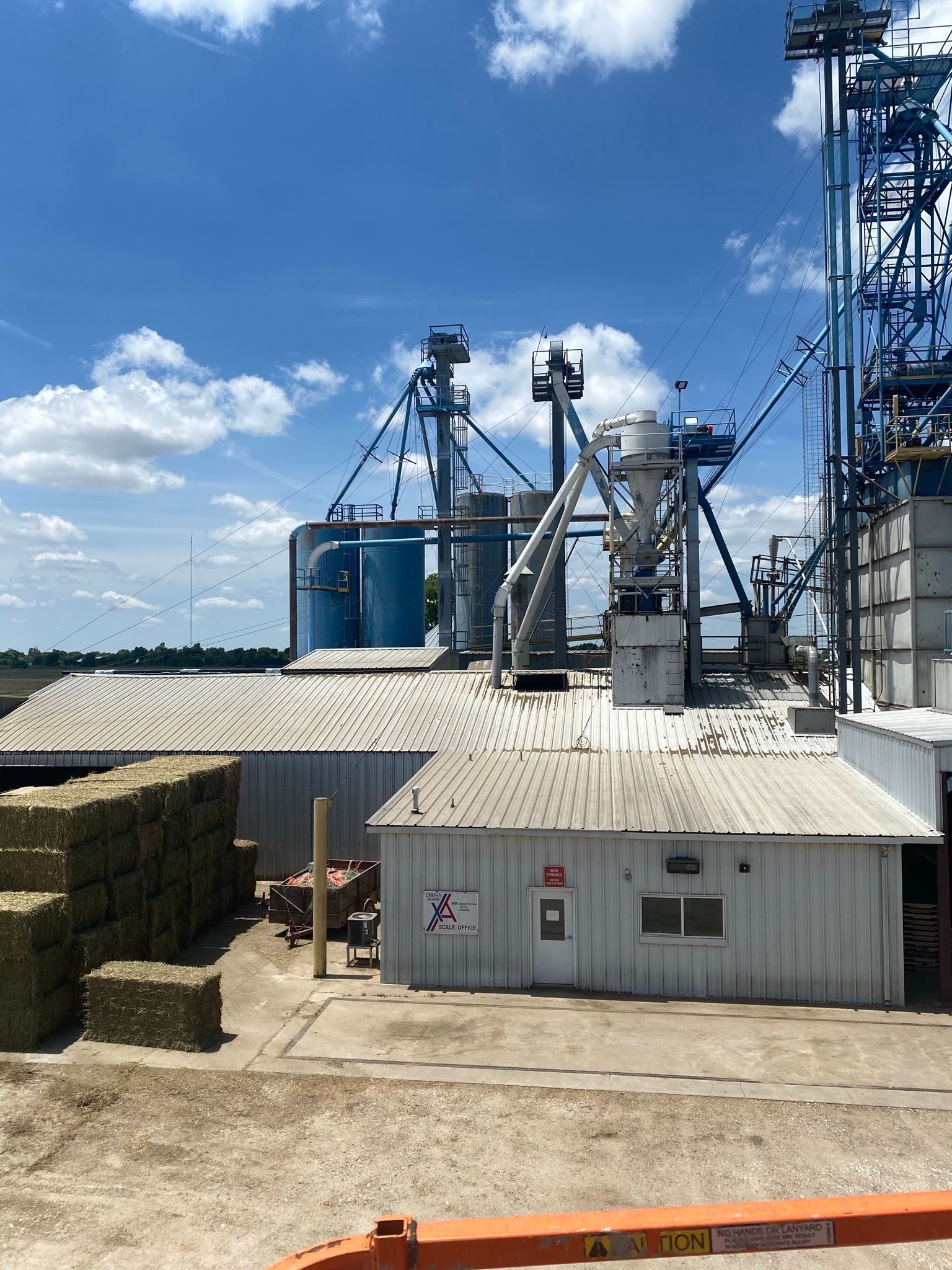 Grain processing facility with silos, buildings, and blue sky.