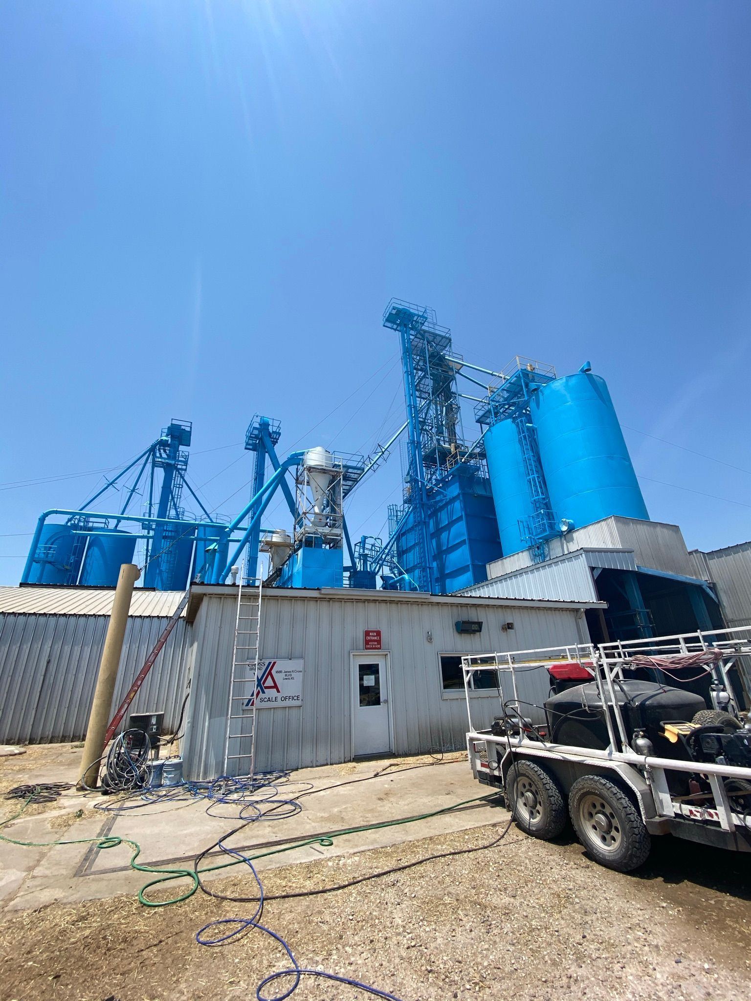 Blue industrial plant with silo, office, and trailer under a bright blue sky.