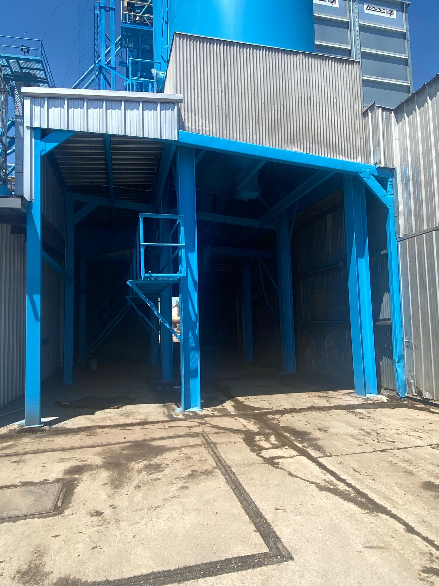 Blue industrial structure with platform and ladder, set on concrete ground.