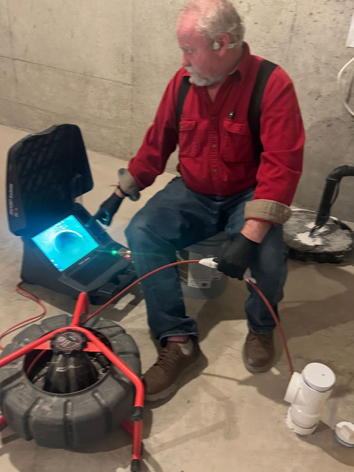 Man inspecting pipes with camera, wearing respirator in a concrete room.