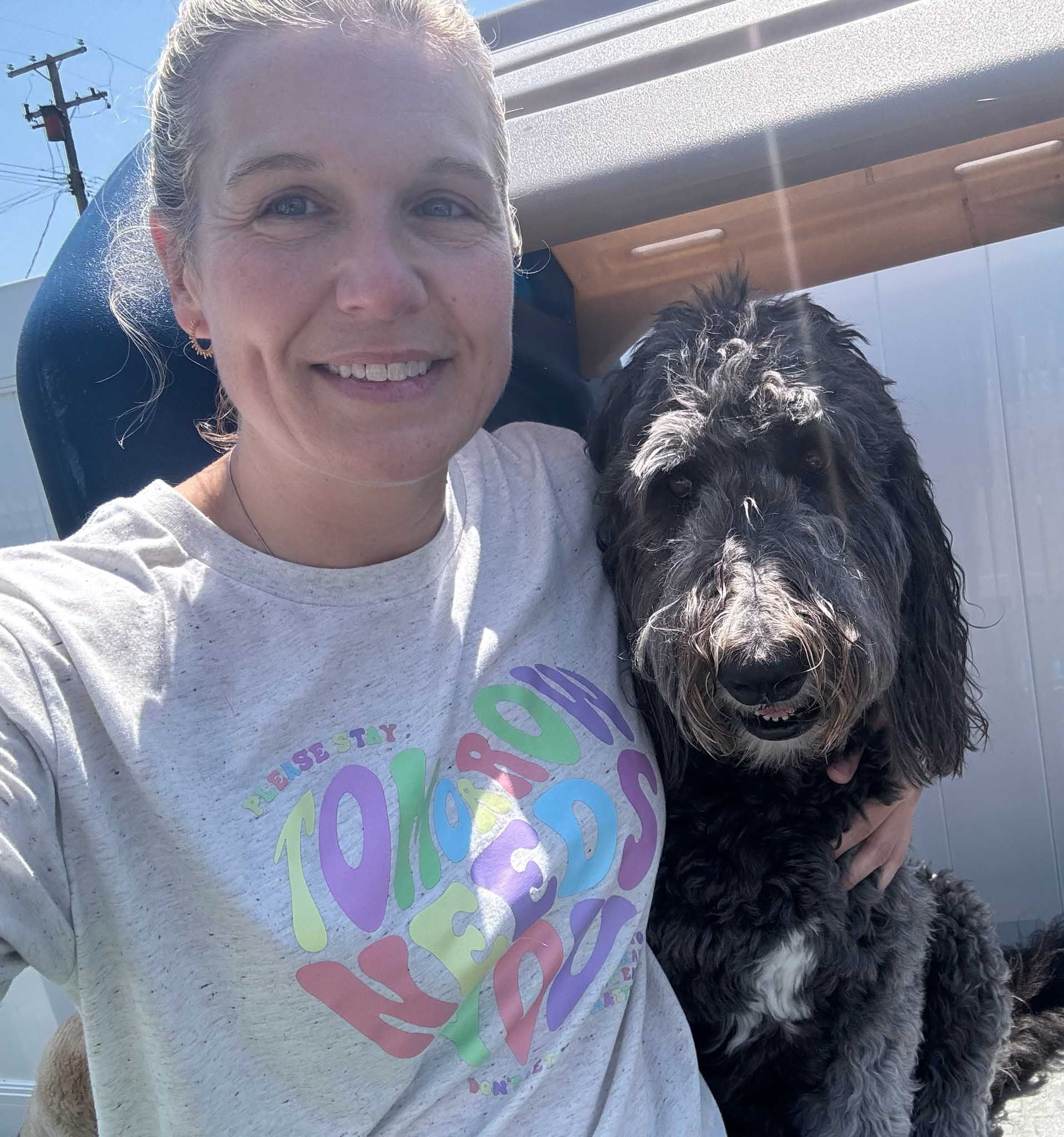 Woman and fluffy black dog smiling outdoors; woman's shirt has a colorful heart design.
