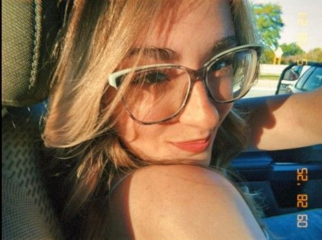 Woman in glasses smiling, lit by sunlight in a car, date stamp 