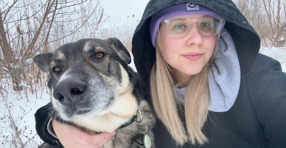 Person in a hooded jacket and a dog pose for a selfie in the snow.