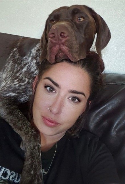 Woman with a brown and white dog resting its head on her head; both looking at the camera.